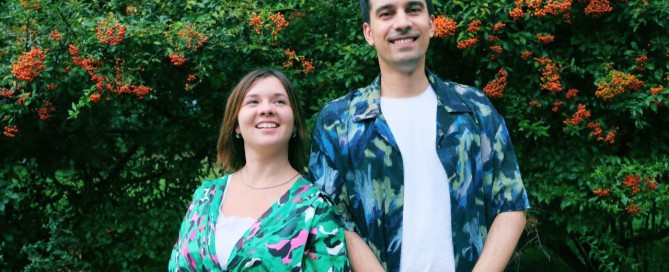 Two journalists stand smiling in a park