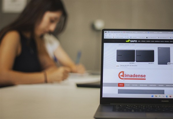Laptop showing Almadense news website in foreground; journalist working in background