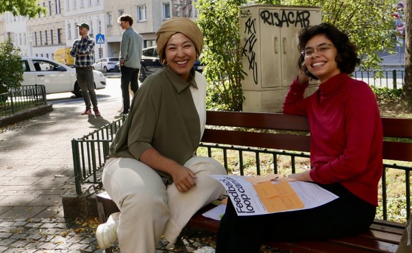 Two female journalists sit smiling in a park